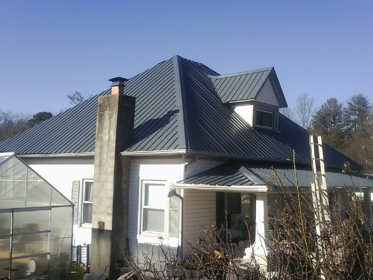 Dark blue standing seam metal roof on a white farmhouse with dormer — Slate & Tile Roof Repair by Roofing Brothers in Eagle Bay