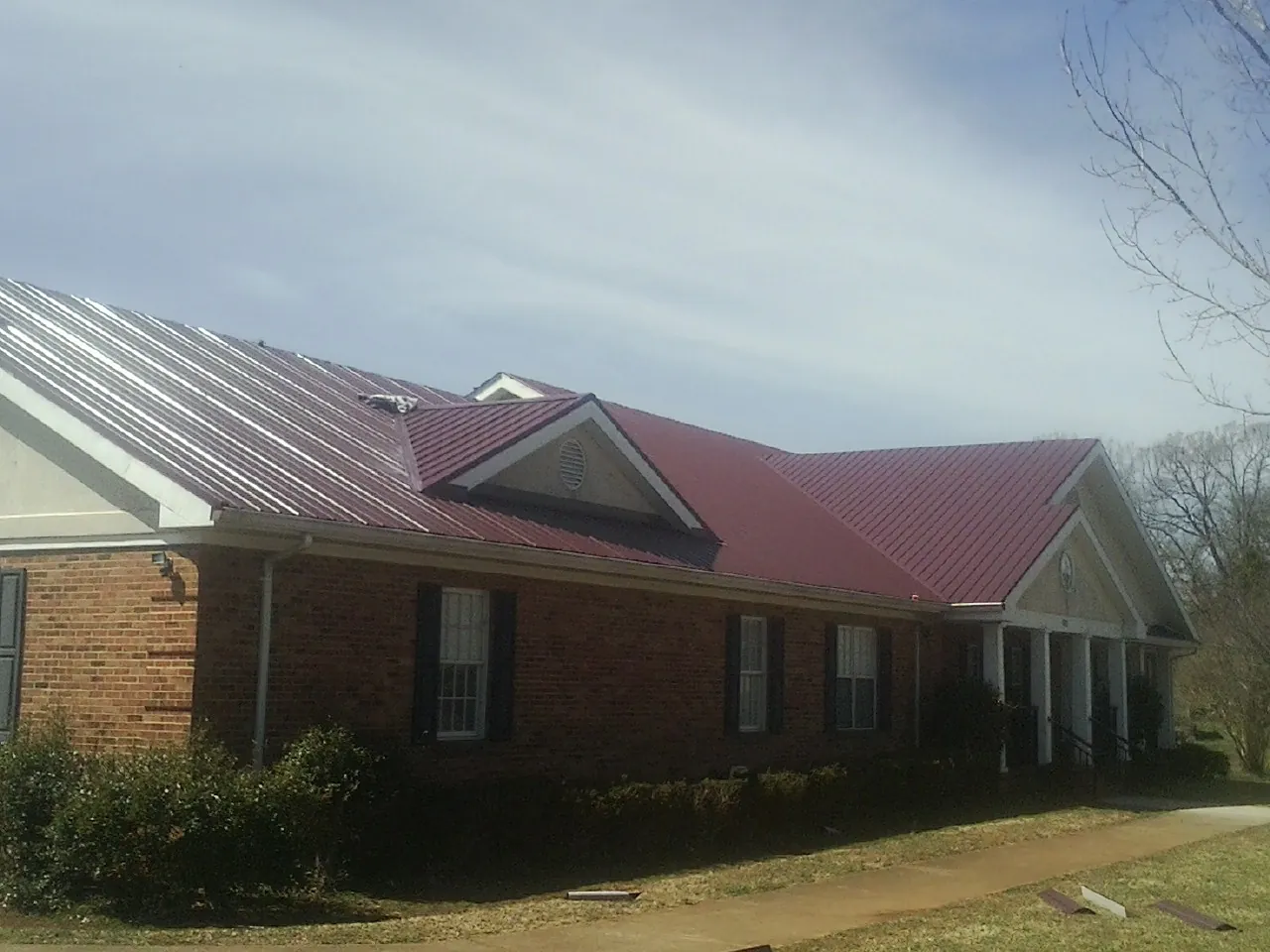 Red metal roof with gabled entries on a long brick building, from a Hail Damage Roof Repair job in Eagle Bay
