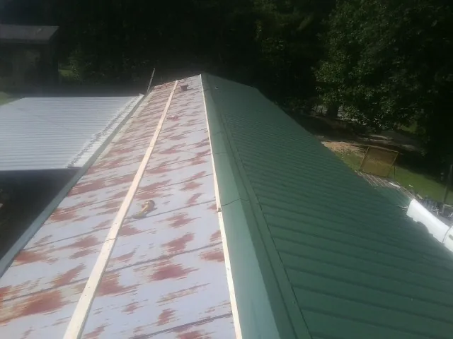 Old rusted panels beside newly installed green metal roofing — Wind Damage Roof Repair by Roofing Brothers in Eagle Bay