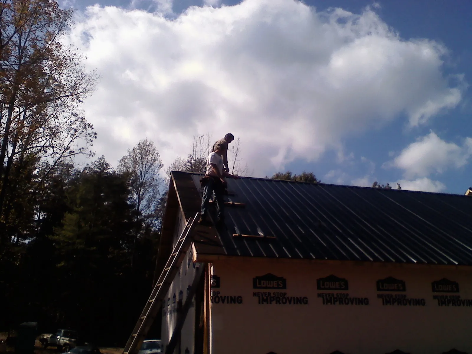 Roofer fastening dark metal panels high against a cloudy sky, from a Roof Inspection job in Eagle Bay