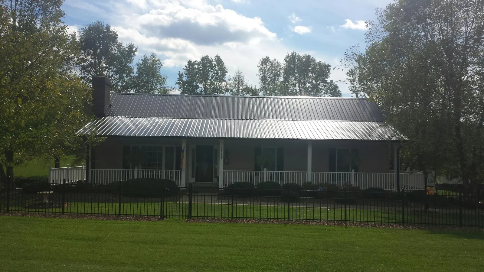 Gray metal roof on a brick ranch with a full width front porch — Gutter Guard Installation work by our crew in Eagle Bay