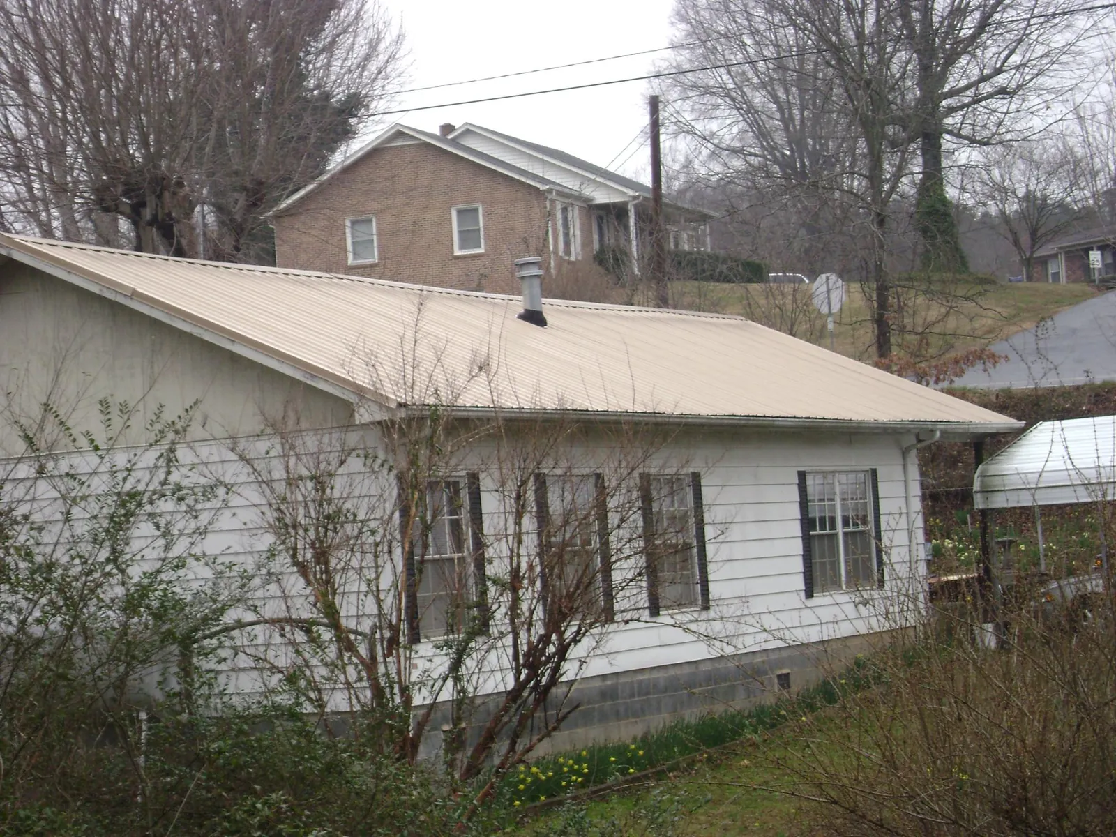 Tan metal roof on a white sided house set into a hillside — Commercial Roofing by Roofing Brothers in Eagle Bay