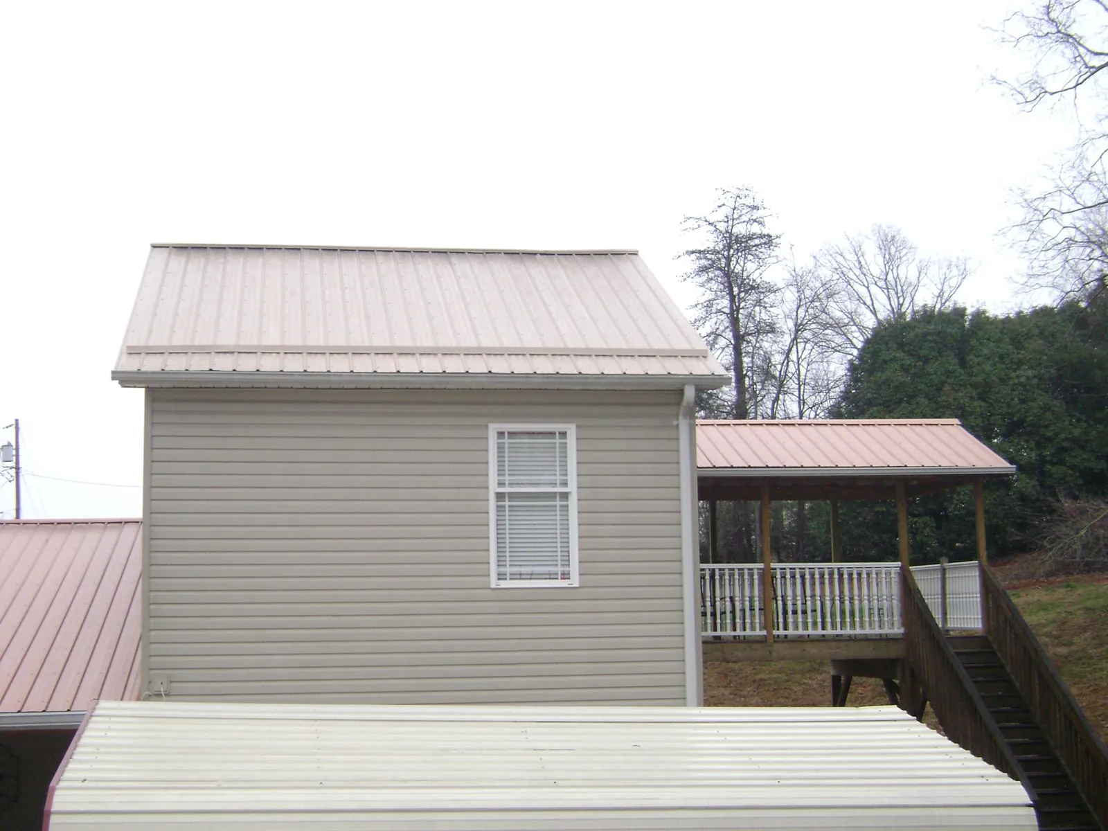Tan metal roofs on a two story addition and attached porch, from a Roof Replacement job in Eagle Bay